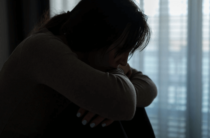 A photo of a woman sitting in a dark room.