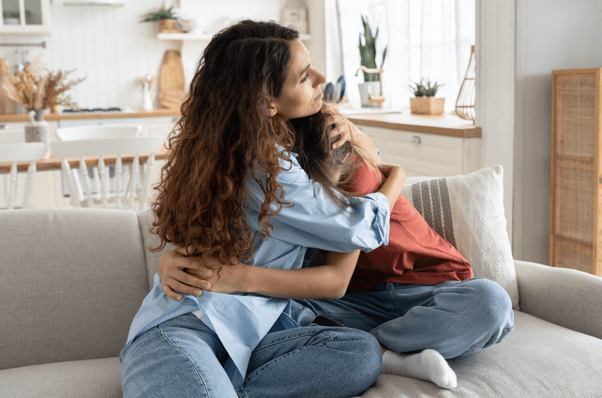 A photo of a mother sitting on the couch with her child, while they are both hugging.