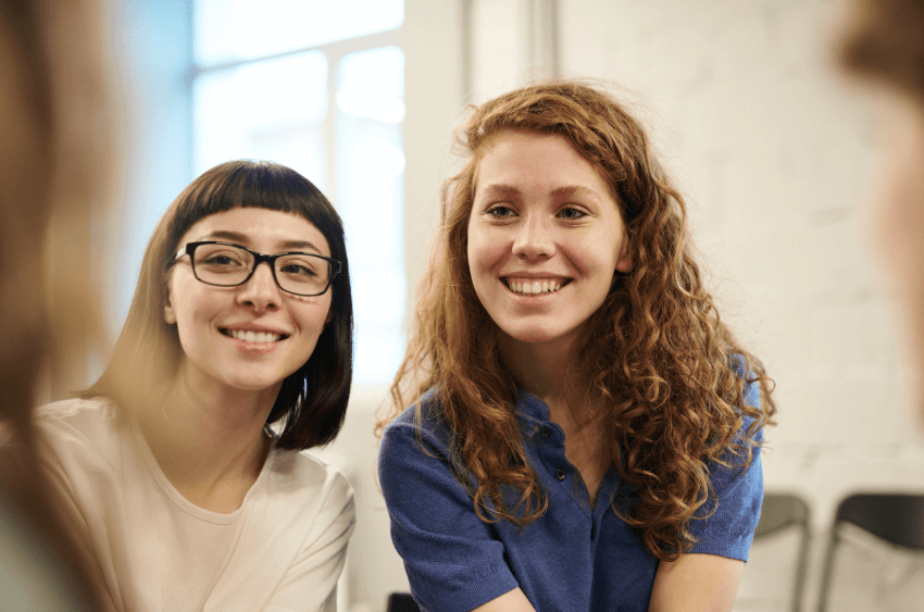 A photo of two young women sitting next to each other, while they are both smiling.