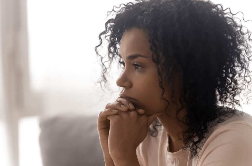 A photo of a woman with a serious look on her face, while holding her face in her hands.