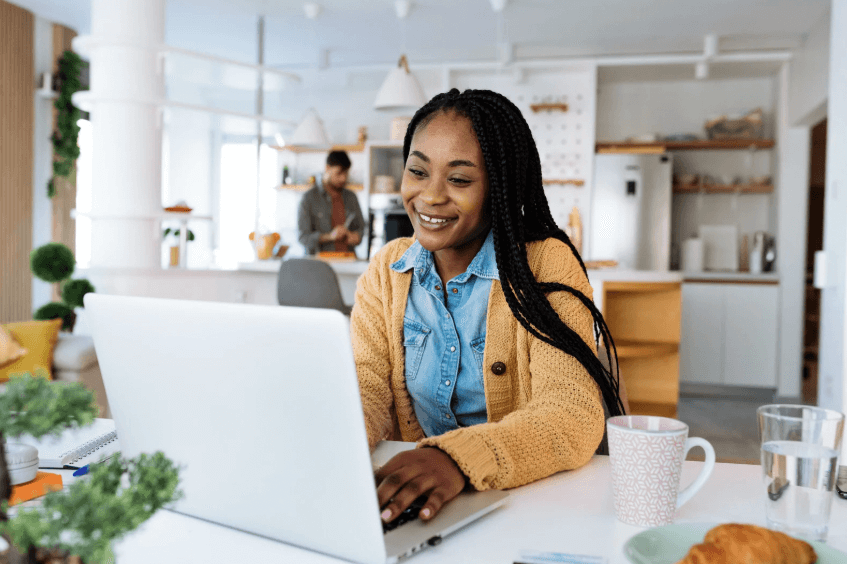 A photo of a woman in a kitchen on a computer, while smiling.