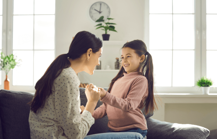 A photo of a mother holding her daughter's hands and talking to each other, while they are both smiling.