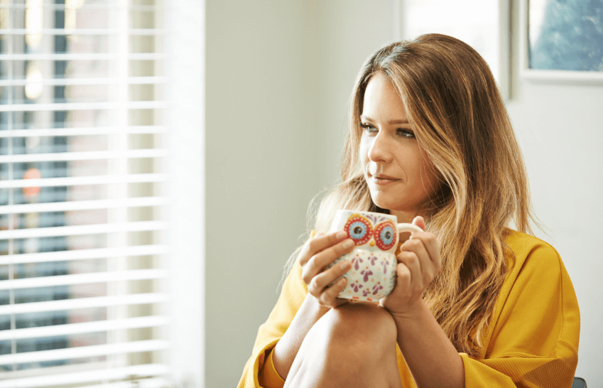 A photo of a woman in a yellow shirt holding a coffee mug, while looking to the left.