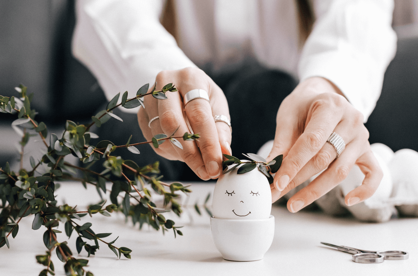 A photo of a woman placing a vine around an egg with a drawn-on smiling face.