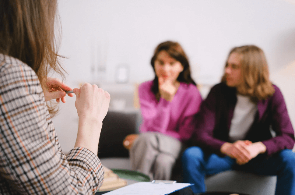 A photo of a woman, portraying a therapist, sitting in front of couple who are blurred.